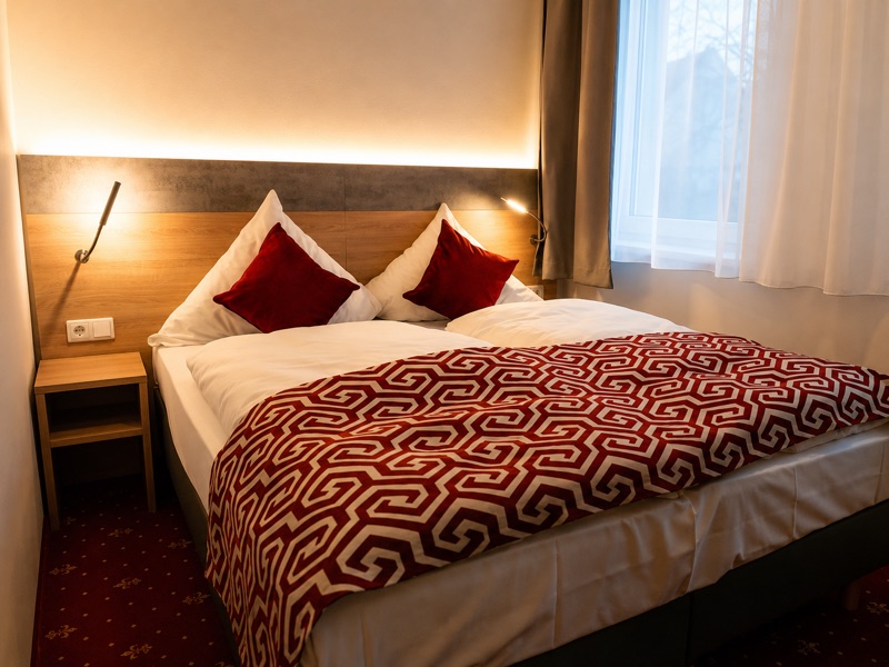 Doppelzimmer mit Doppelbett, roter Tagesdecke und Fenster